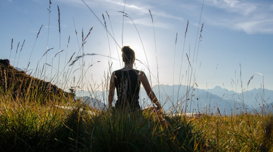 Frau sitz auf einem Stein in grüner Berglandschaft