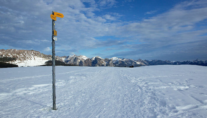 Wegweiser im Schnee und Sicht auf Berge in der Sonne